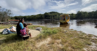 two women sitting on a grassy hill by a body of water