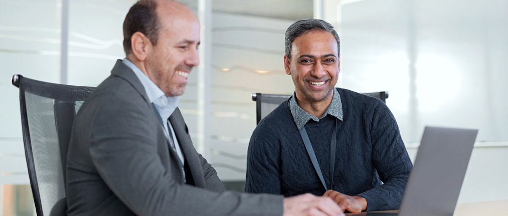 a couple of men sitting at a table looking at a laptop