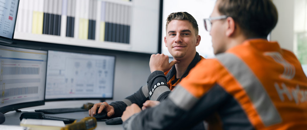 a person sitting at a desk with another man looking at him