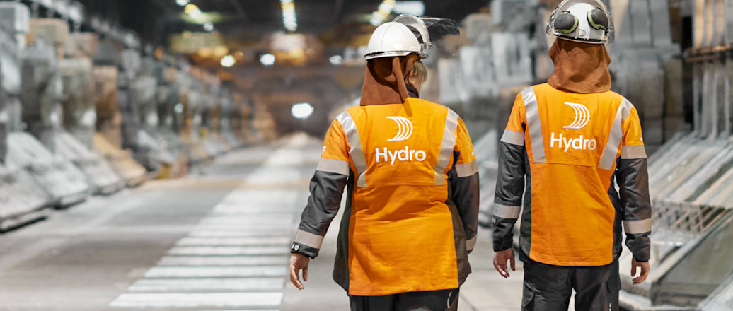 a couple of men wearing safety vests and helmets walking down a street