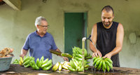 a couple of men stand near each other holding bananas